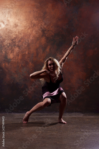 Fototapeta Naklejka Na Ścianę i Meble -  Full-length photo of dancing blonde girl looking in camera in short black dress on brown background