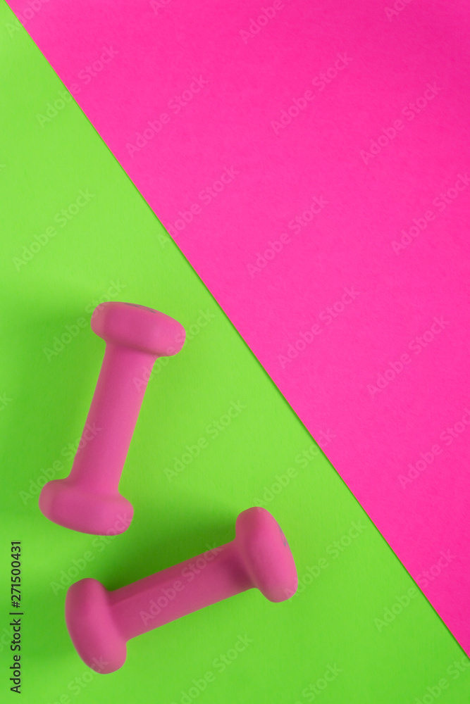 Fitness equipment with womens pink weights/ dumbbells isolated on a lime green and hot pink background with copyspace Fitness equipment with womens pink weights/ dumbbells isolated on a lime green and hot pink background with copyspace