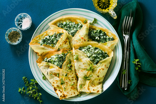 Traditional Italian pancakes crepes with spinach and ricotta on a served blue table. healthy vegetarian diet photo