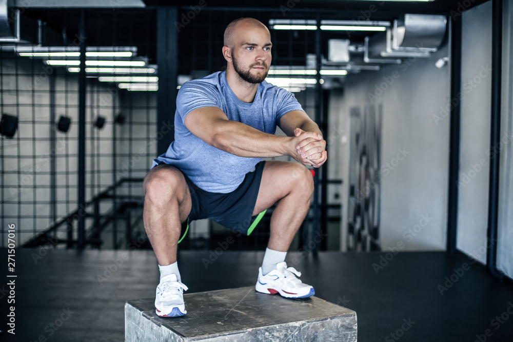 Man doing squats on a squat box at the gym. guy at the gym working out standing on a wooden squat box. dressed in a sports uniform. Man doing squats on a squat box at the gym. guy at the gym working out standing on a wooden squat box. dressed in a sports uniform.