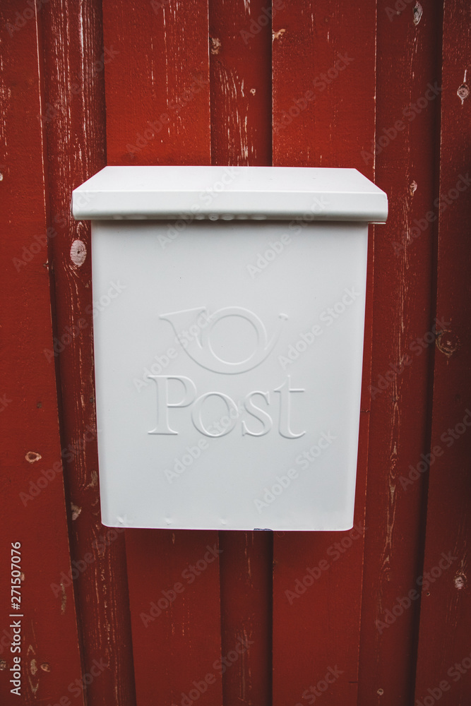 A white mailbox on a red wooden wall with a red door A white mailbox on a red wooden wall with a red door