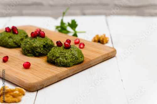 Spinach balls Pkhali with walnuts and served with pomegranate on white wooden background