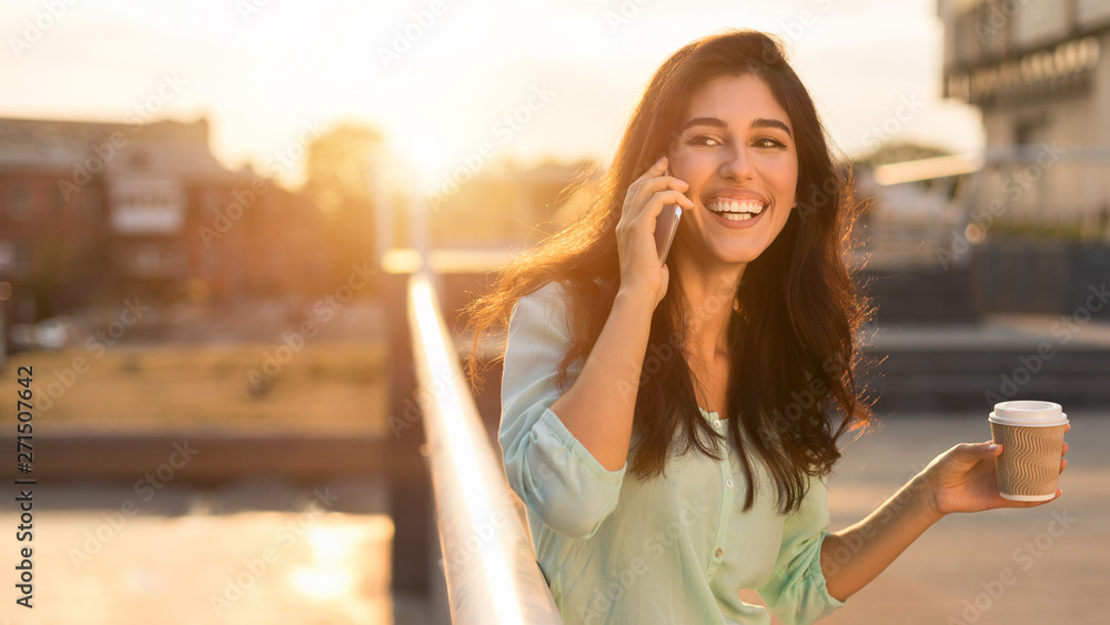 Happy woman talking on phone and drinking takeaway coffee