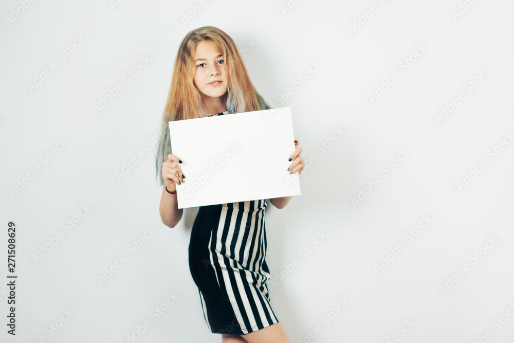 Naklejka premium Girl and mockup poster, gray background. Beautiful teen girl wearing striped dress holding in her hands blank canvas.