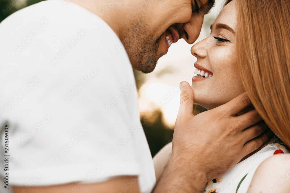 Fototapeta premium Close up portrait of a beautiful caucasian couple smiling face to face with closed eyes before kissing outside against sunset while dating .