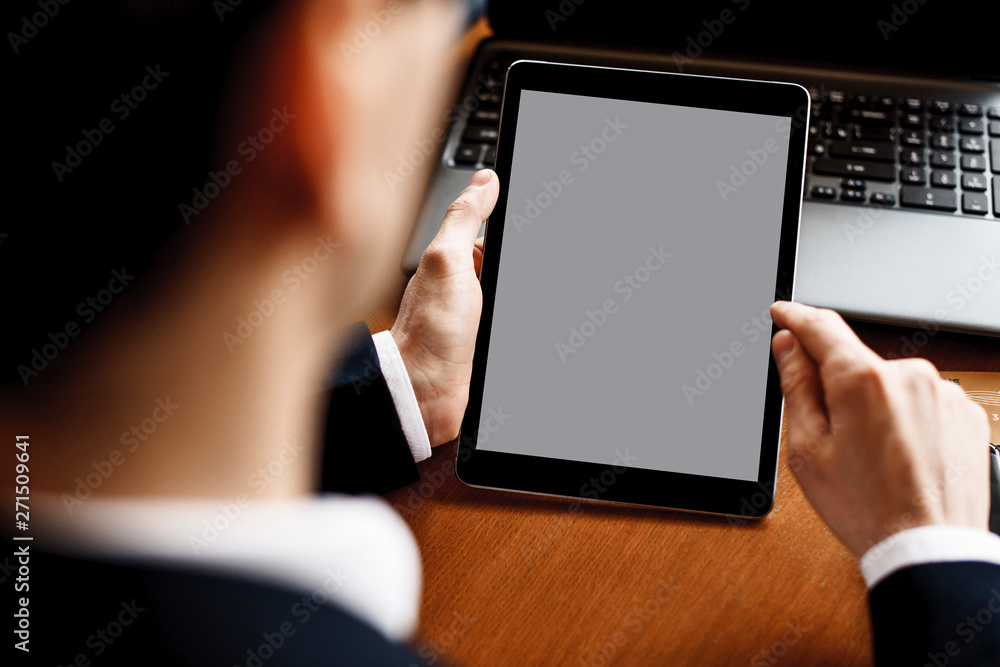 Male hands using a tablet while sitting at a desk with a laptop on it.