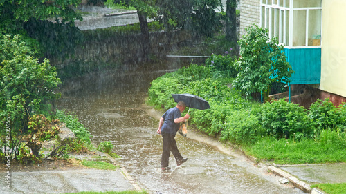 A man with an umbrella jumps over a puddle during heavy rain in summer