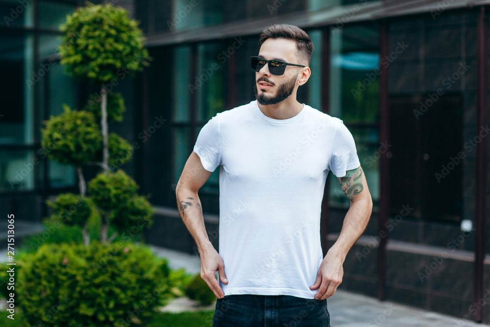 A young stylish man with a beard in a white T-shirt and glasses. Street photo A young stylish man with a beard in a white T-shirt and glasses. Street photo