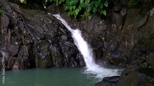 Serene shot of a gorgeous waterfall flowing over a rocky ledge in the forest, Saut d'Acomat in Guadeloupe photo