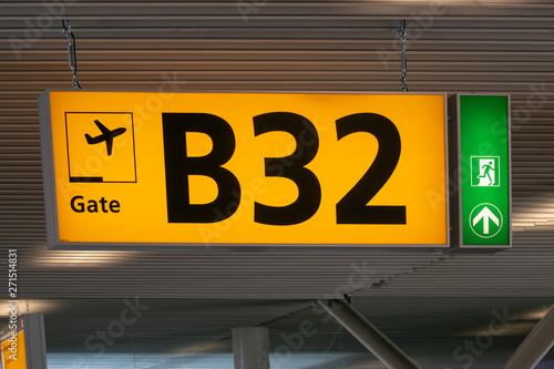 Yellow illuminated airport gate number sign with emergency exit indicator