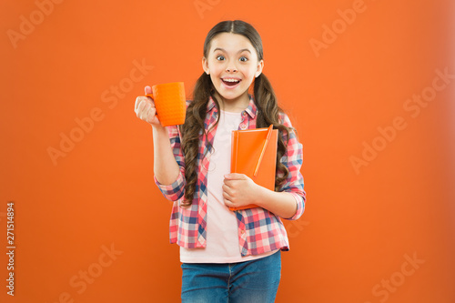 Fueled for school. Small girl enjoying her school break on orange background. Happy schoolgirl having school breakfast in morning. Cute school child smiling with cup and note book