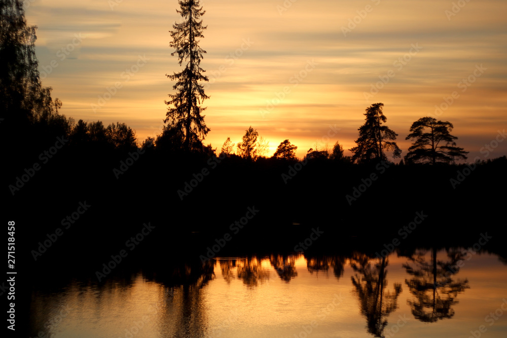Background Siluet forests near the lake. The sunset sky and tall trees are reflected in the water.