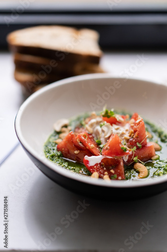 Italian cuisine dish, burrata with fresh red tomatoes in green pesto sauce, olive oil and cashew nuts. All in white bowl with golden cutlery and pieces of black toasted bread. Lunchtime snack in cafe.
