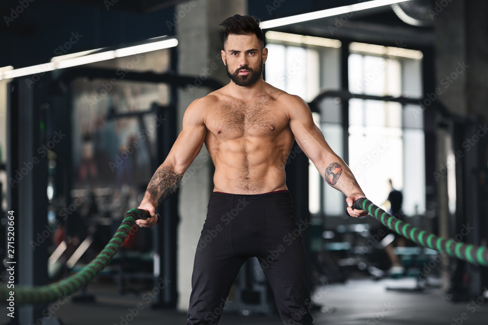 Muscular guy with naked torso exercising with battle ropes