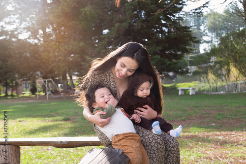 young mother having fun with her two children in her arms smiling and watching each other in the park outdoors photo