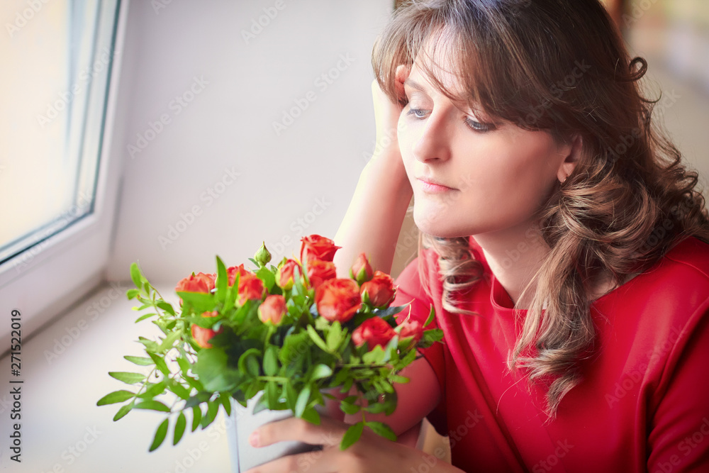 A young teacher is sad at the window at graduation. The woman at the school on farewell to students. Teacher with a bouquet of red roses. A young teacher is sad at the window at graduation. The woman at the school on farewell to students. Teacher with a bouquet of red roses.