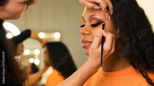 Makeup artist draws arrows on eyelids of african girl. Evening make-up. Closeup portrait side view photo