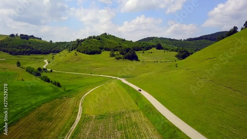 Aerial Footage of an relaxing and peaceful green landscape of a driving car on a countryside road surrounded by green hills in Transylvania. 4K. photo