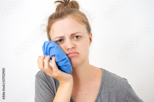 Young caucasian woman holds ice bag to her cheek, suffering from a toothache or dental surgery