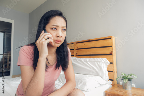 Upset woman is having a phone conversation on her bed.