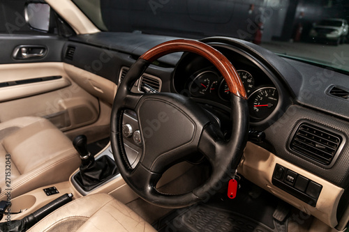 Close-up of the dashboard, speedometer, tachometer and steering wheel with wooden inserts with phone setting and volume buttons. Luxurious car interior details.