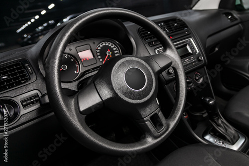 Close-up of the dashboard, speedometer, tachometer and steering wheel with phone setting and volume buttons. Luxurious car interior details.