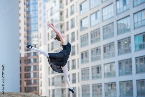 Ballerina in tutu posing against a residential building. Beautiful young woman in black dress and pointe shoes jumping with incredible flexibility. Ballerina performs elegant jumping with deflection.