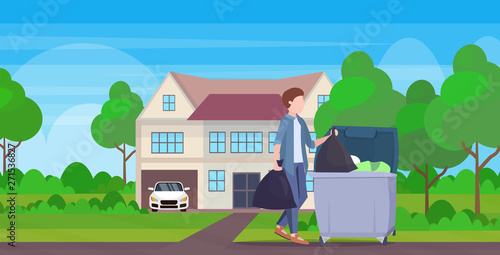 man putting two garbage bags in trash bin young guy doing housework cleaning service concept modern village house exterior full length flat landscape background horizontal