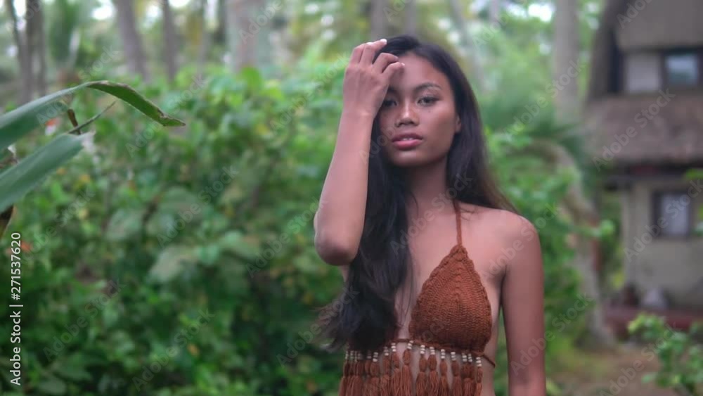 beautiful asian model in brown knitted top stands on tropical path near cottage beautiful asian model in brown knitted top stands on tropical path near cottage