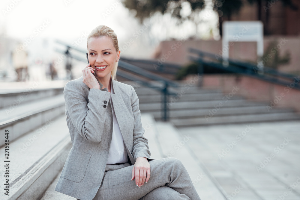 Positive businesswoman in formal wear sitting on the stairs in the city and talking on the phone. Positive businesswoman in formal wear sitting on the stairs in the city and talking on the phone.