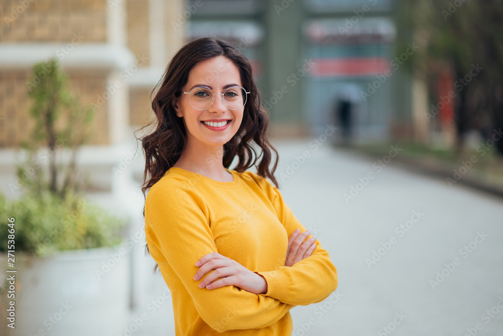 Portrait of a young confident woman outdoors, smiling at camera. - obrazy, fototapety, plakaty 