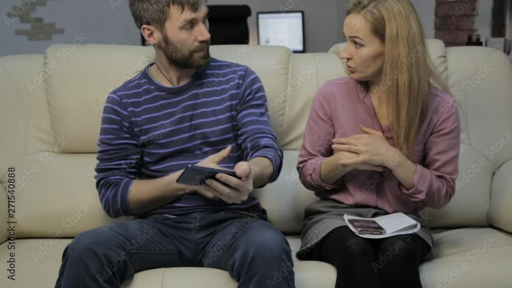 blonde student reads her notes, and her boyfriend sitting on sofa and uses smartphones blonde student reads her notes, and her boyfriend sitting on sofa and uses smartphones