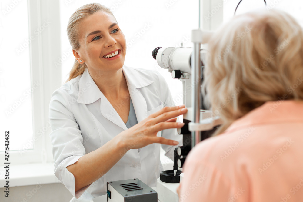 Laughing positive ophthalmologist in white uniform working with short-haired patient Laughing positive ophthalmologist in white uniform working with short-haired patient