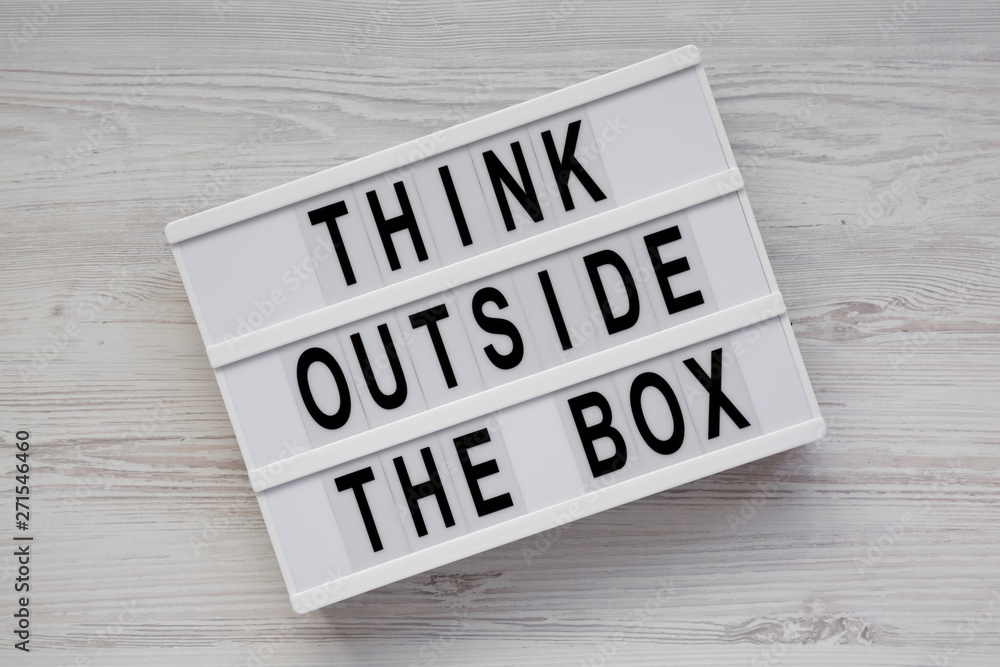 Light box with 'Think outside the box' words on a white wooden surface, top view. Flat lay, overhead, from above. Close-up. Light box with 'Think outside the box' words on a white wooden surface, top view. Flat lay, overhead, from above. Close-up.