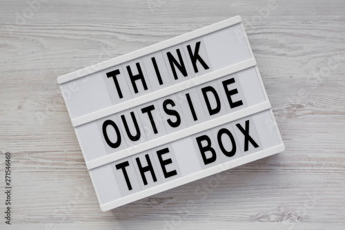 Light box with 'Think outside the box' words on a white wooden surface, top view. Flat lay, overhead, from above. Close-up.