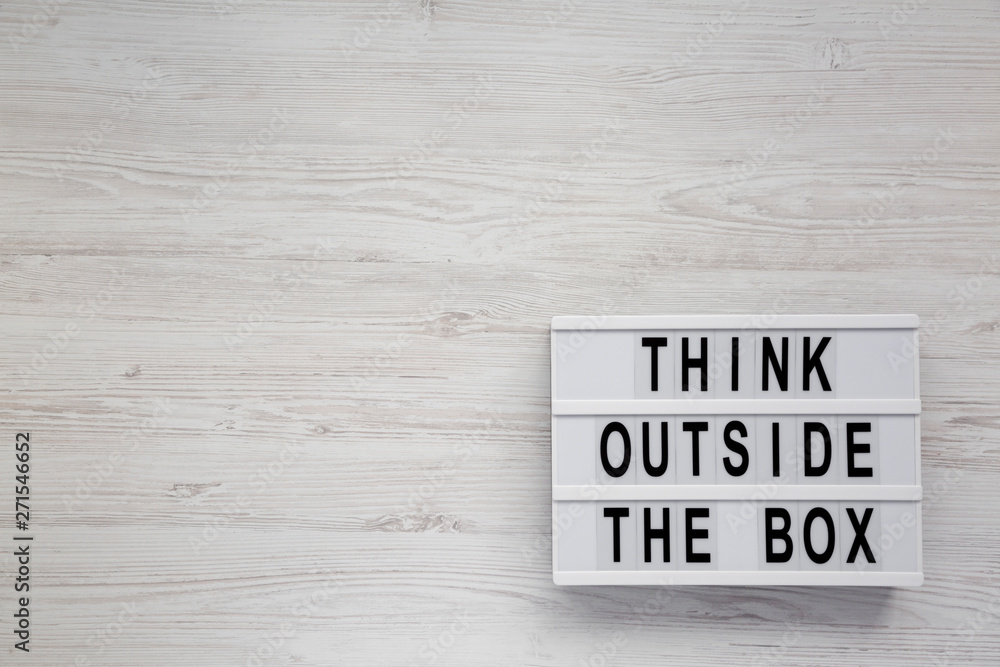 'Think outside the box' words on a modern board on a white wooden surface, top view. Flat lay, overhead, from above. Copy space. 'Think outside the box' words on a modern board on a white wooden surface, top view. Flat lay, overhead, from above. Copy space.