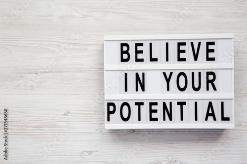 'Believe in your potential' words on a modern board on a white wooden background, top view. Copy space.