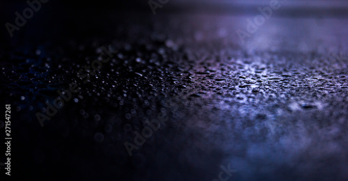Dark background. Spilled liquid on the mirror surface, the reflection of neon lights, glare, blurred bokeh background. Neon, night view of the streets of a big city.