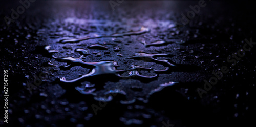 Dark background. Spilled liquid on the mirror surface, the reflection of neon lights, glare, blurred bokeh background. Neon, night view of the streets of a big city.