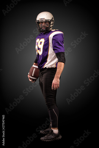 American football player posing with ball on black background