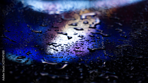 Dark background. Spilled liquid on the mirror surface, the reflection of neon lights, glare, blurred bokeh background. Neon, night view of the streets of a big city.