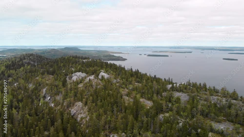 Aerial, drone shot, towards Paha-Koli and Akka-Koli peaks, over spring colored forests, lake Pielinen, in the background, on a cloudy day, in Koli national park, North Karelia, Finland