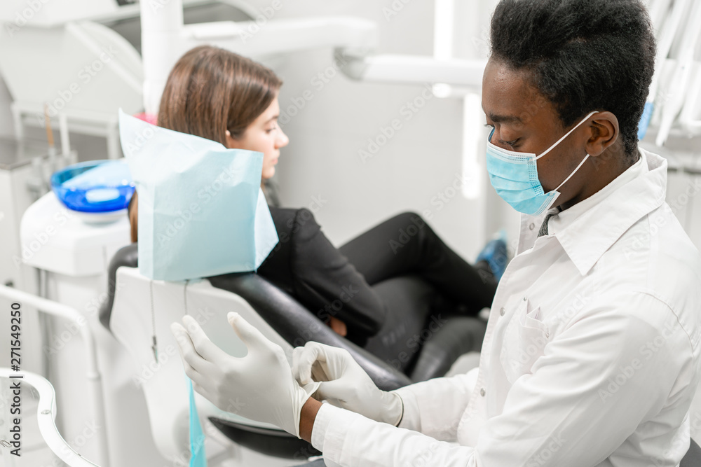 Fototapeta premium Young African male dentist with a patient. Woman in the dentist chair at dental clinic. Medicine, health, stomatology concept. dentist treating a patient.