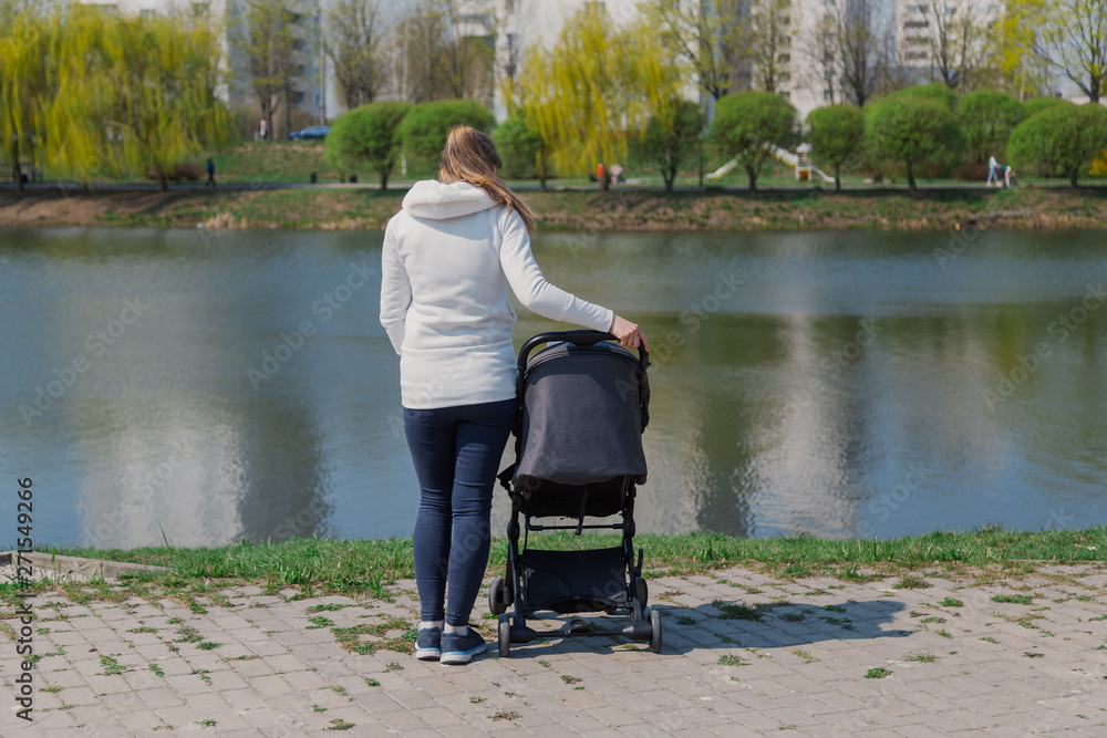 Young mother with a baby in a stroller by the lake in summer. Young mother with a baby in a stroller by the lake in summer.