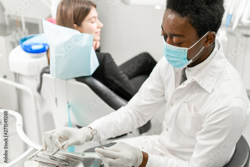 Young African male dentist with a patient. Woman in the dentist chair at dental clinic. Medicine, health, stomatology concept. dentist treating a patient.