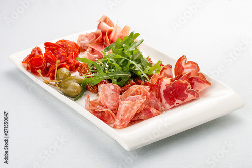 Appetizers of Italian sausages. Prosciutto, chorizo, pancetta and salami. Capers, arugula and sun-dried tomatoes. On white background
