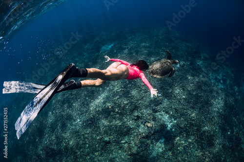 Young woman freediver with fins swim underwater with sea turtle.