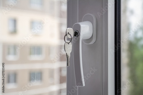 The concept of protecting a child from falling out of windows. Handle with a lock on the window. Apartment house on the background. Closeup, selective focus