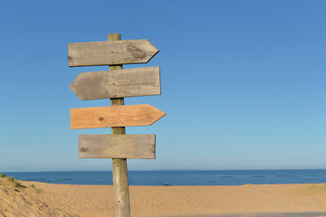 wooden signs on a post in a beach under blue sky