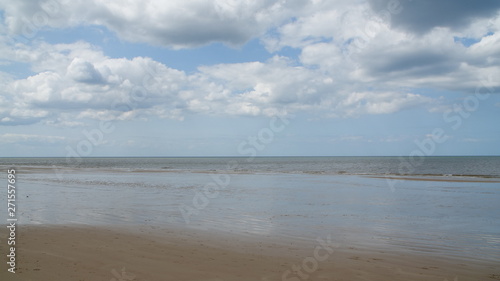 A perfect sandy beach with clear water, small sea waves and bright blue sky with some beautiful white clouds